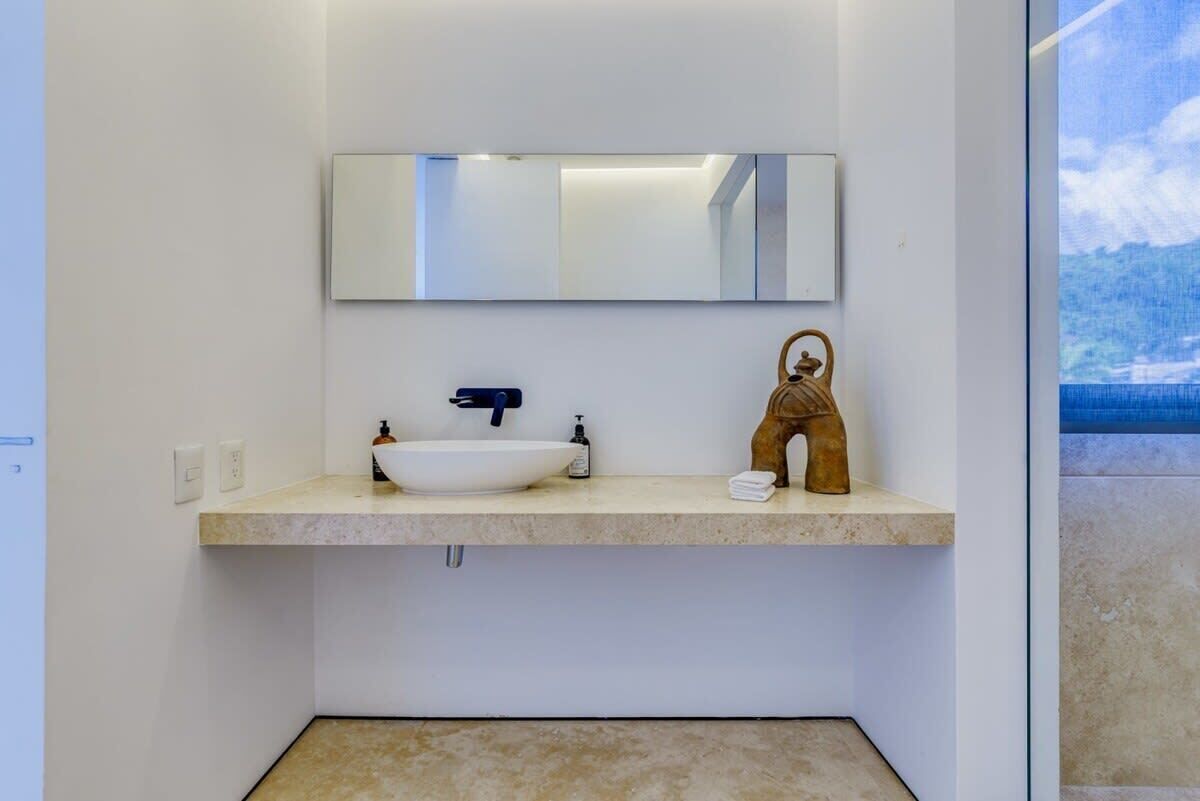 A modern bathroom with a white sink, a mirror, and a small statue.