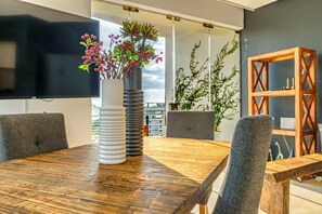 Une salle de réunion moderne avec une table en bois, des chaises grises à revêtement en tissu, un vase blanc contenant des plantes et une bibliothèque en bois.