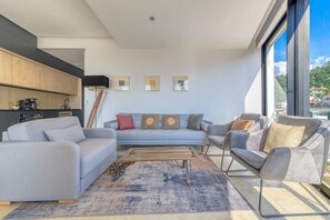A modern living room with a sofa, armchairs, a coffee table, and a view through large windows.