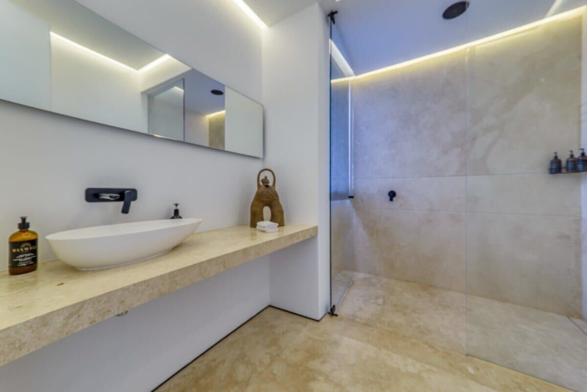 A modern bathroom with a large mirror, a white sink, and a shower area.