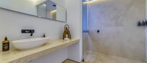 Un baño moderno con un espejo grande, un lavamanos blanco y una zona de ducha.
