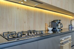 Une cuisine moderne équipée d’une cuisinière à gaz, d’une machine à café et d’appareils électroménagers en acier inoxydable.
