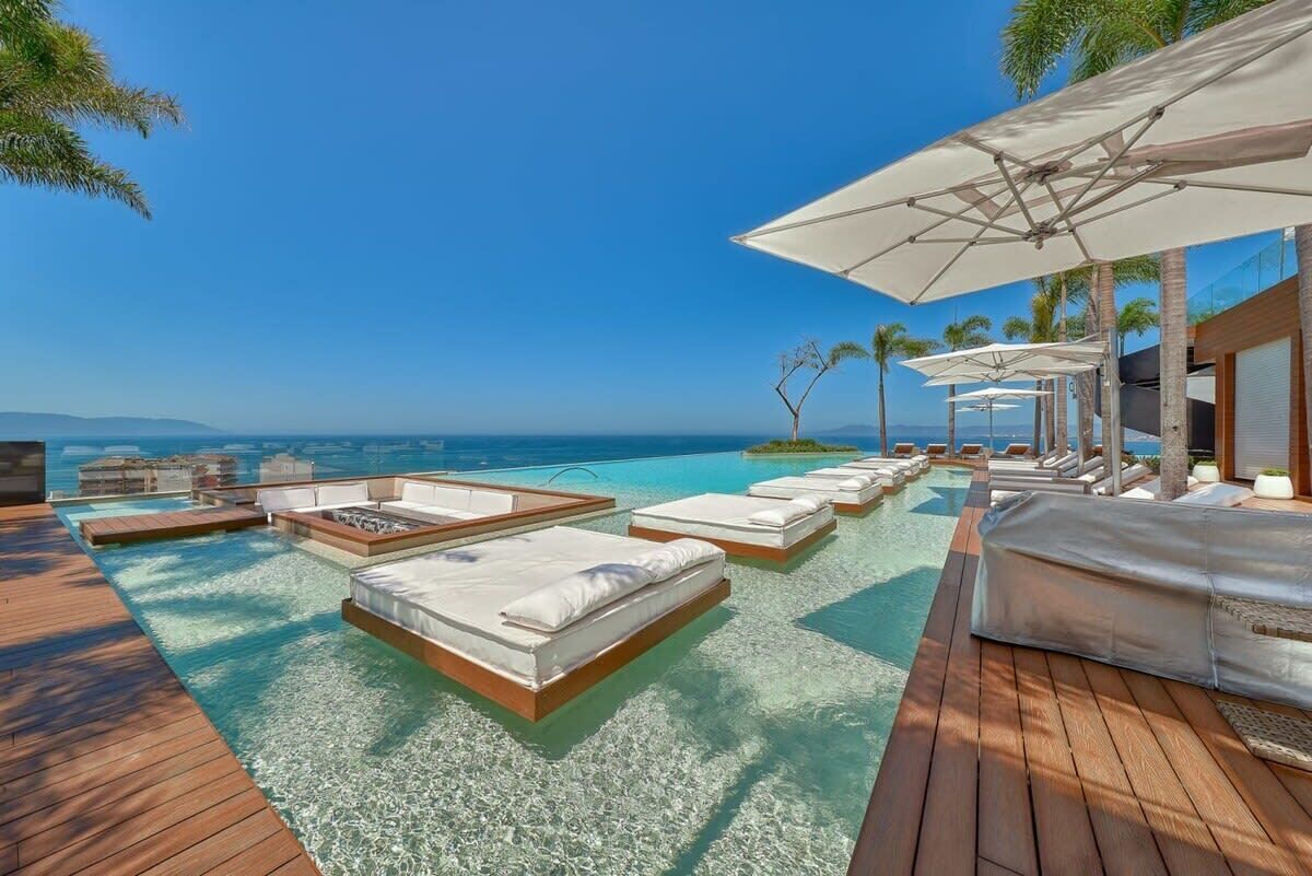 A poolside area with lounge chairs and umbrellas, overlooking a clear blue sea.
