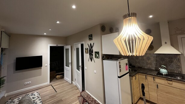 A modern kitchen with a built-in refrigerator, a dining area with a sofa, and a TV mounted on the wall. - One bedroom flat in the center of Riga (Riga)
