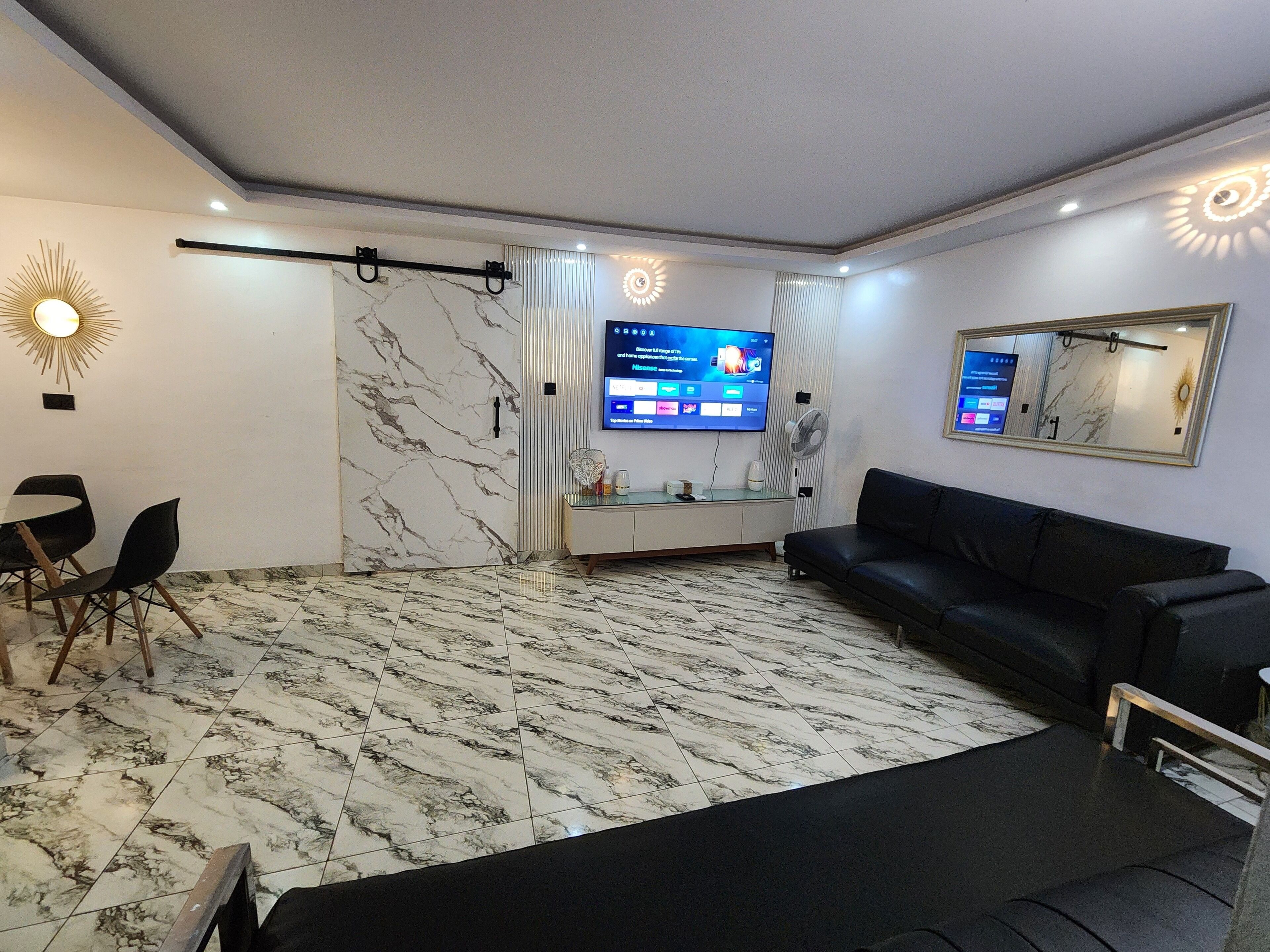 Una sala moderna con televisor, sofá de cuero negro y comedor con sillas.