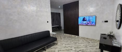 A modern living room with a black sofa, a TV mounted on the wall, and a marble-patterned floor.