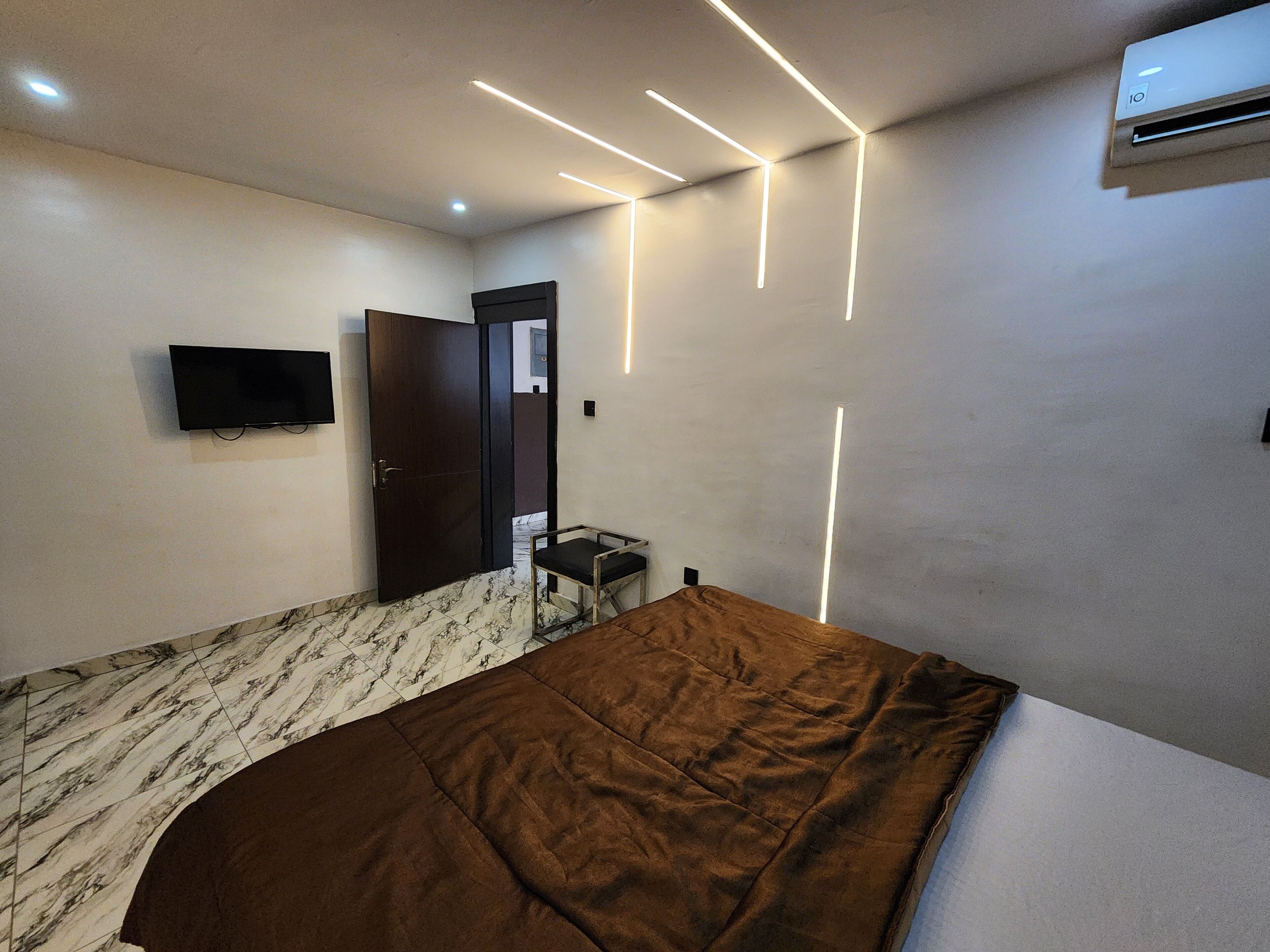 A bedroom with a bed, a TV mounted on the wall, a door, and an air conditioning unit.