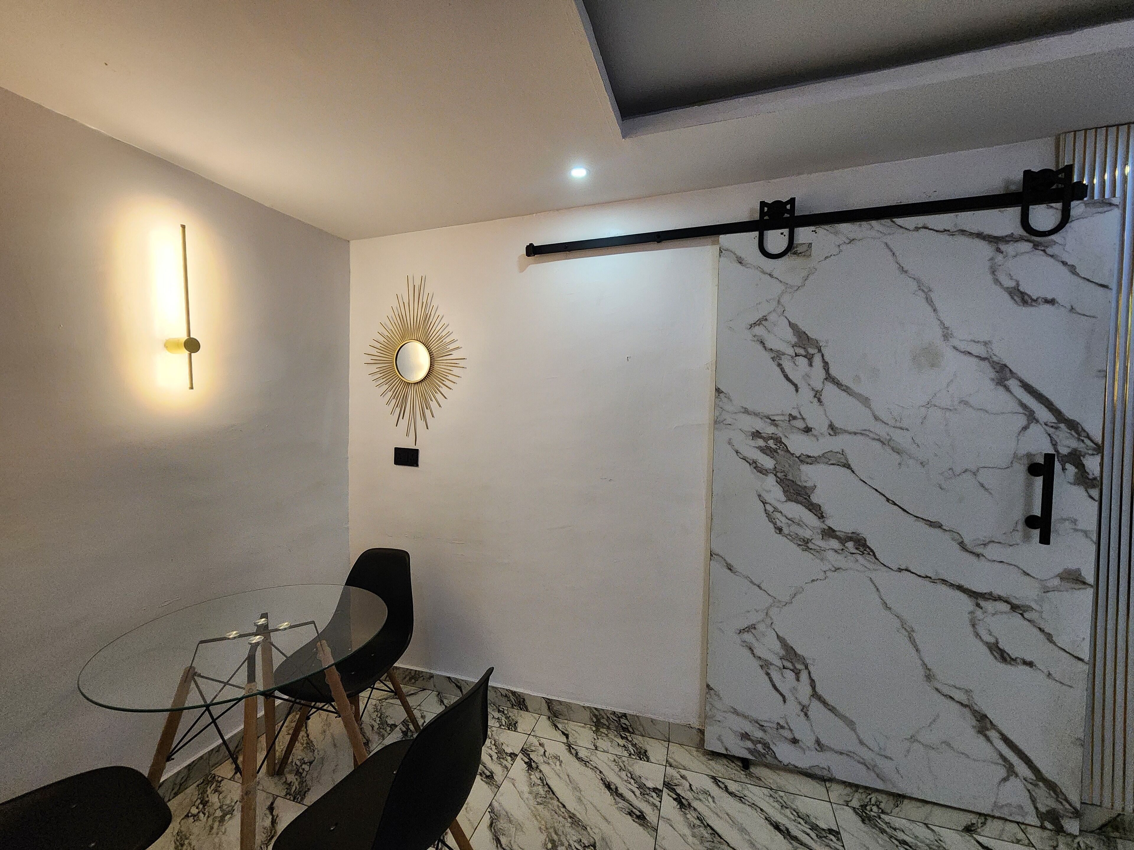 A modern interior with a marble wall, a sunburst mirror, and a minimalist seating arrangement.