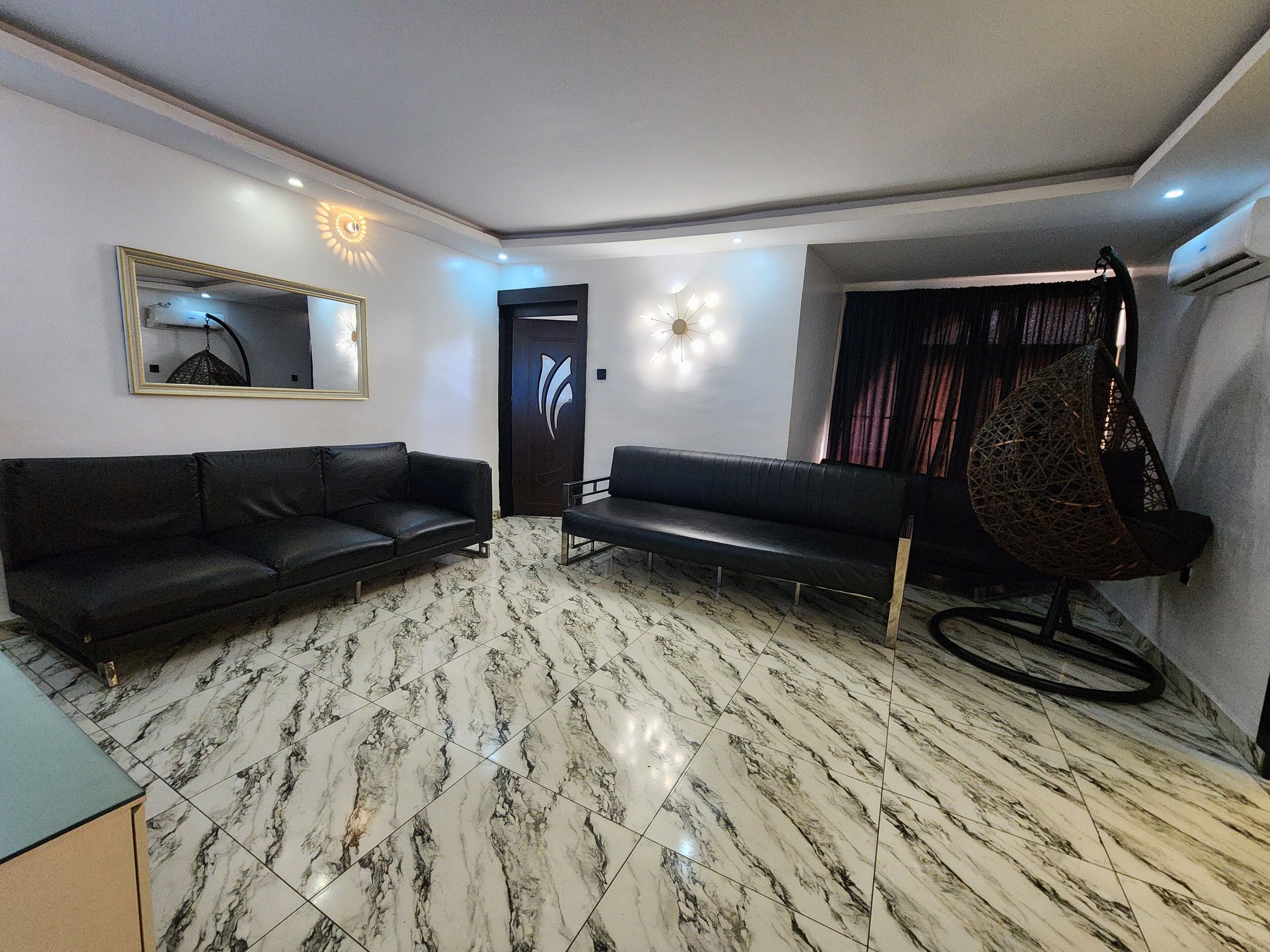 A living room with two black sofas, a hanging chair, and a marble floor.