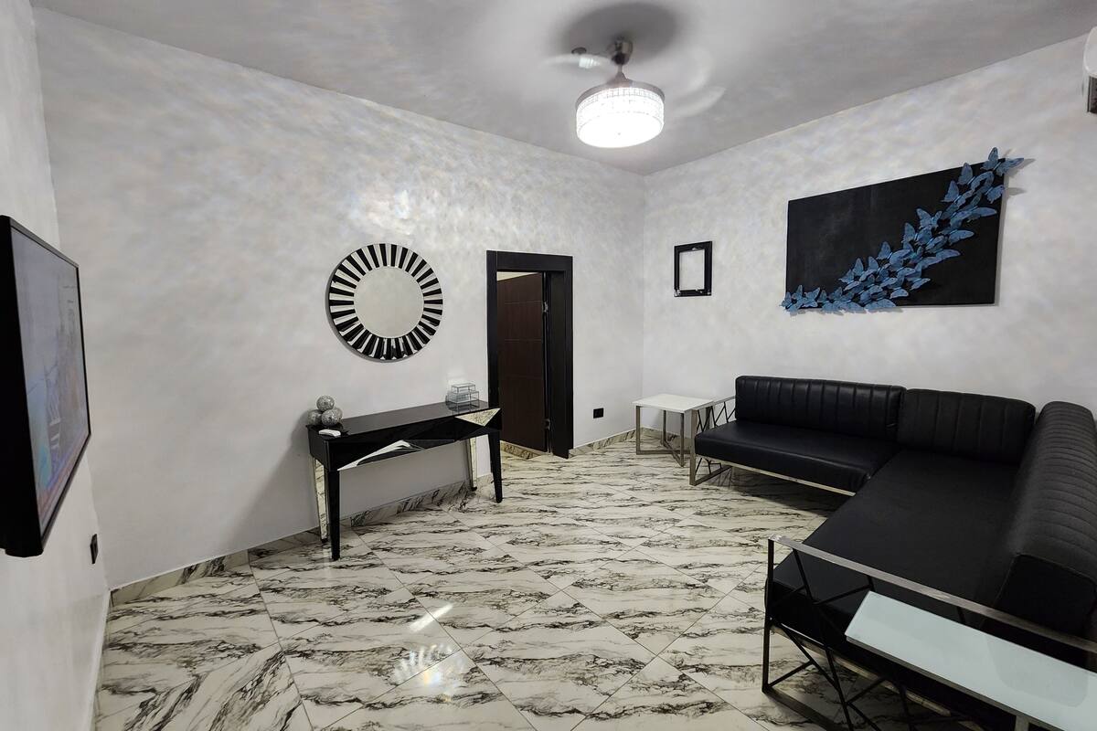 A modern living room with a black sofa, a white coffee table, a black console table, a round mirror, and a blue abstract painting on the wall.