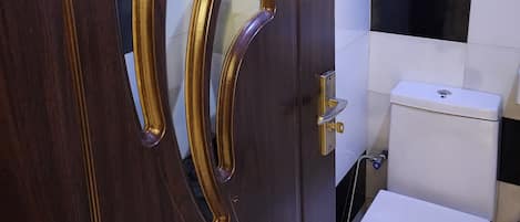 A wooden door with a gold handle and a glass panel, a toilet, and a tiled wall with black and white tiles.