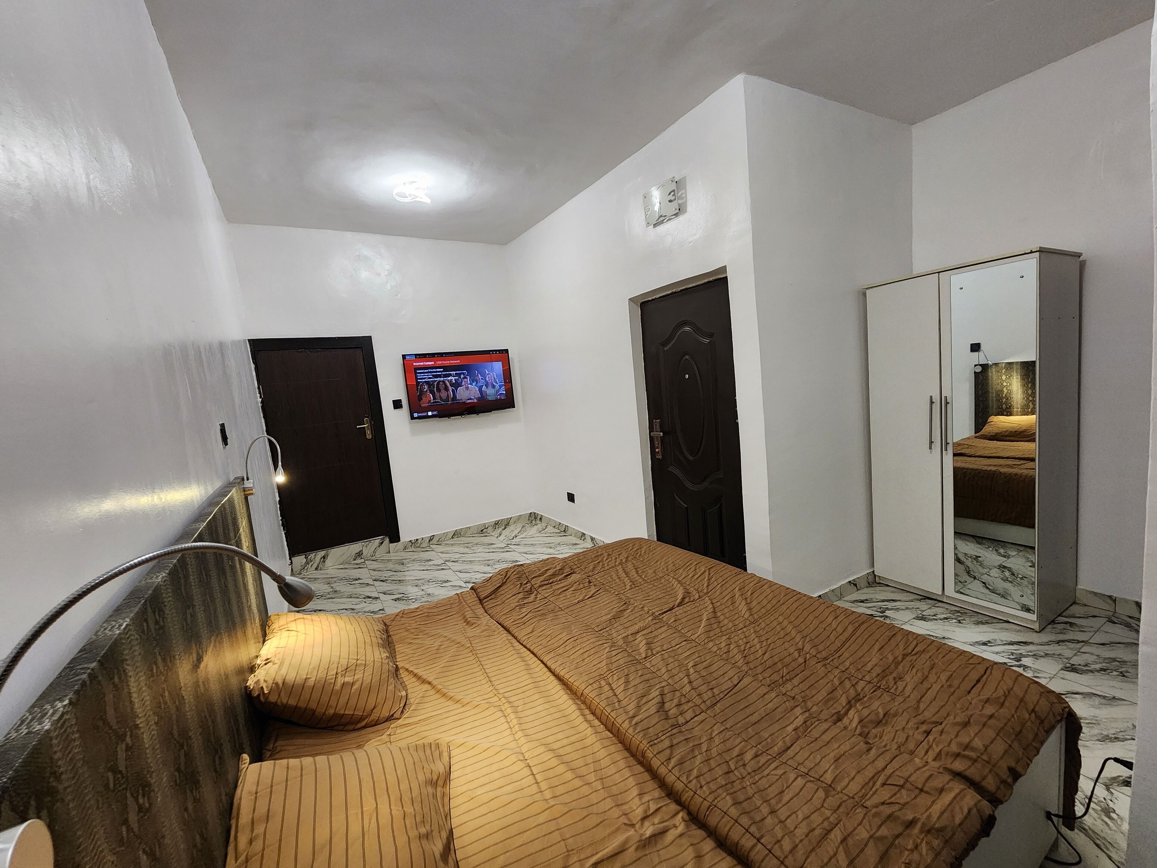 A bedroom with a bed, a wardrobe, a television on the wall, and a door.
