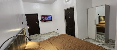 A bedroom with a bed, a wardrobe, a television on the wall, and a door.