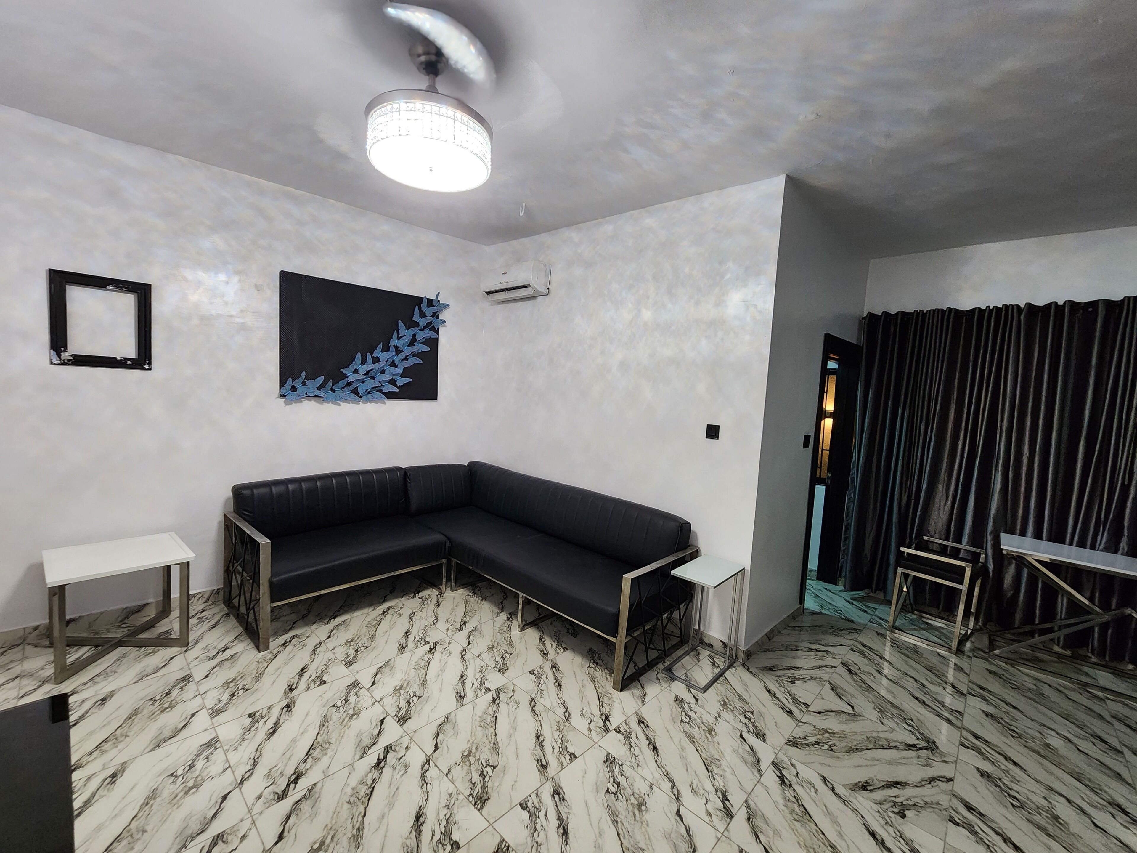 Una sala de estar moderna con un sofá seccional negro, una mesita auxiliar blanca y un suelo con estampado de mármol.
