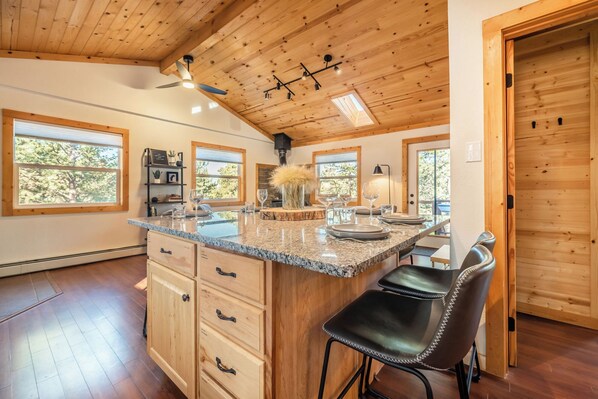 A spacious kitchen with a large island, wooden ceiling, and large windows.