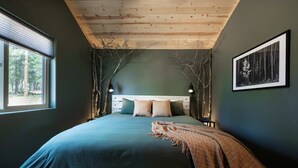 Een slaapkamer met een groot bed, een houten plafond en uitzicht op bomen door een raam.