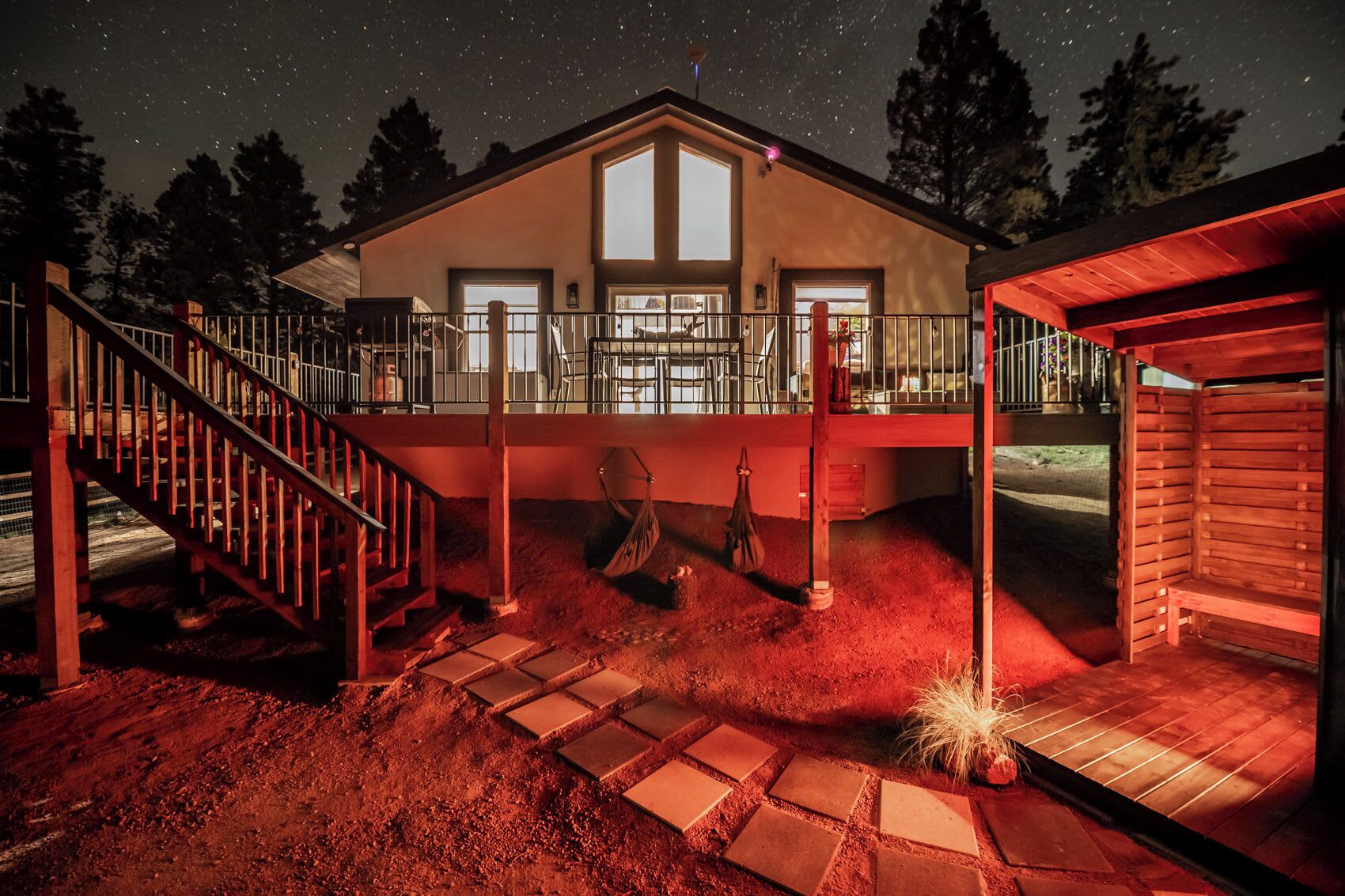 Een huis met een trap naar een terras, een overdekt buitenverblijf en uitzicht op de nachthemel.
