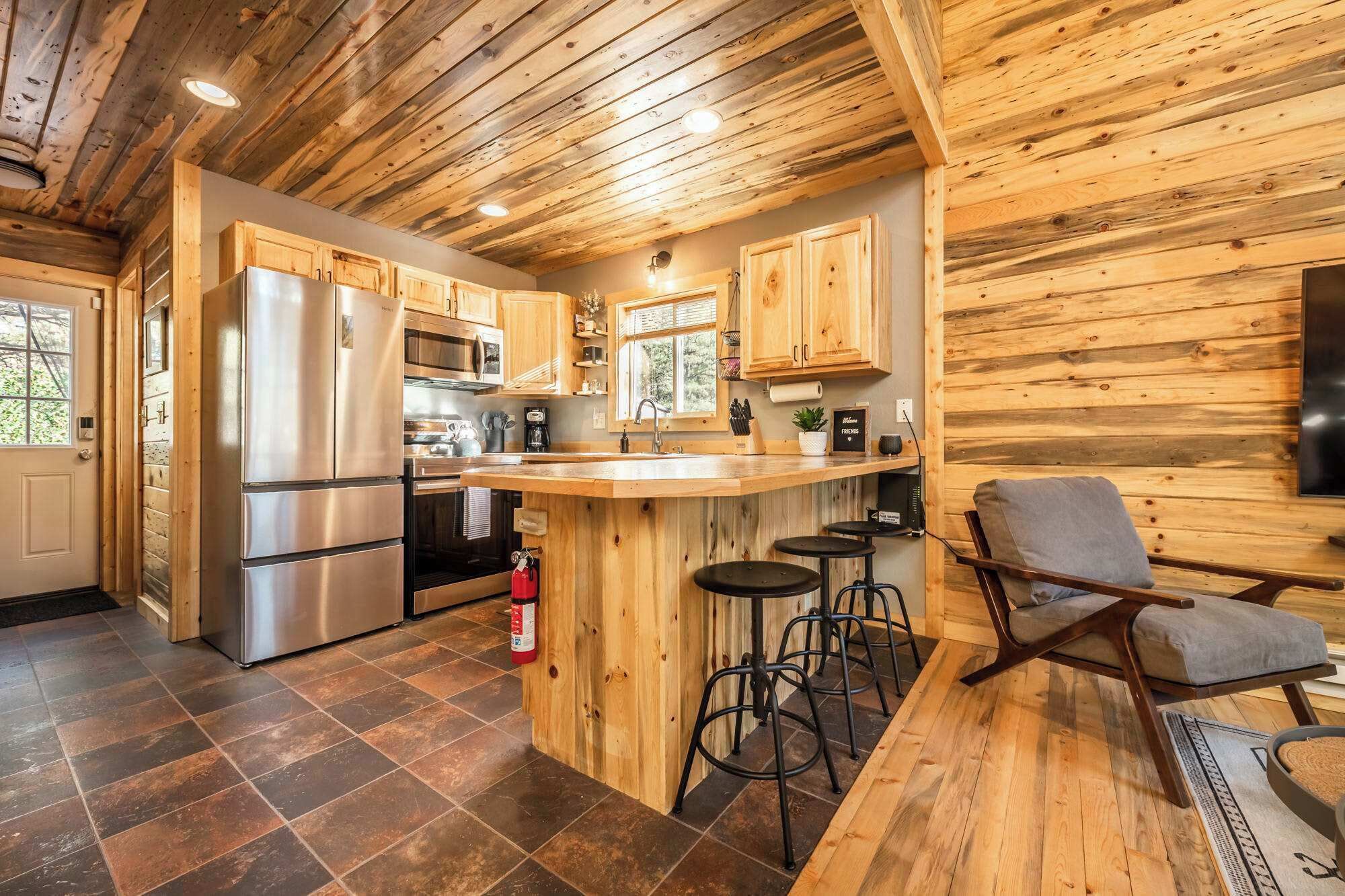 A kitchen with wooden cabinetry, stainless steel appliances, and a bar area with stools.