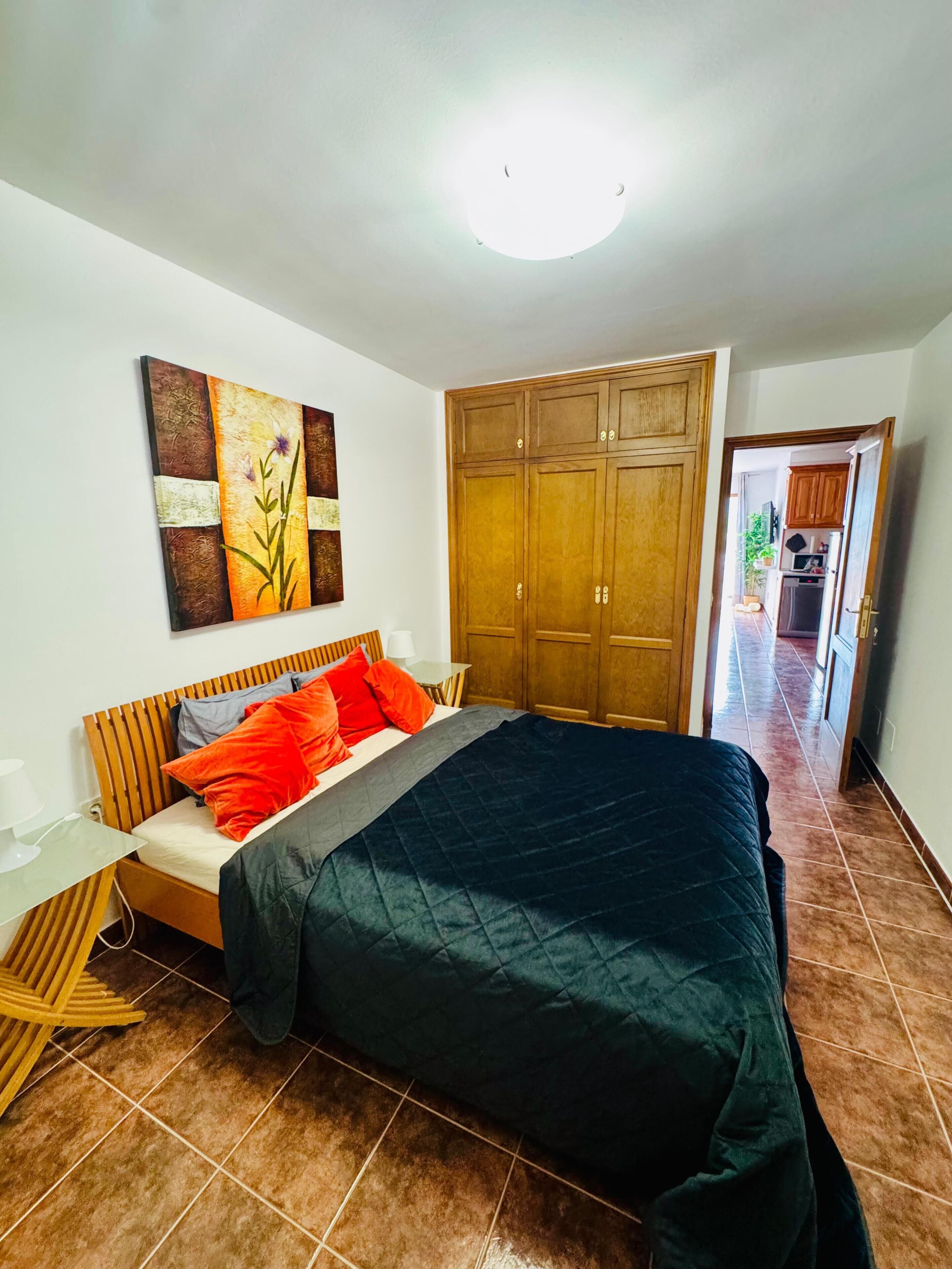 A bedroom with a bed, wooden wardrobe, and a painting on the wall.