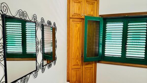 Een slaapkamer met een bed, een houten garderobe, een klein houten tafeltje en twee spiegels aan de muur.