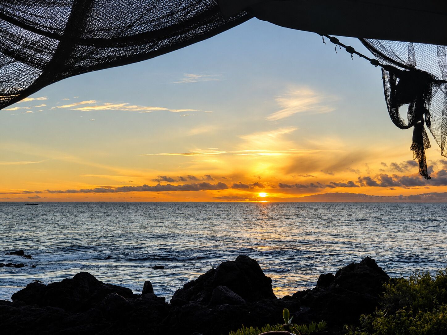A sunset over the ocean with rocks in the foreground.