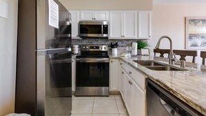 A modern kitchen with stainless steel appliances, white cabinets, and a granite countertop.