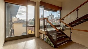 Interior moderno com escada de madeira, amplas janelas com vista para a cidade e piso de azulejos.