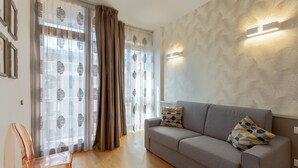 Sala de estar moderna com sofá cinza, cortinas estampadas e uma cadeira transparente.