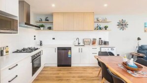 A modern kitchen with white cabinets, a black dishwasher, and a wooden dining table with chairs. - New, family friendly warm /3bedroom3bathroom/kingbed, mountain view/unitB (Lake Tekapo)