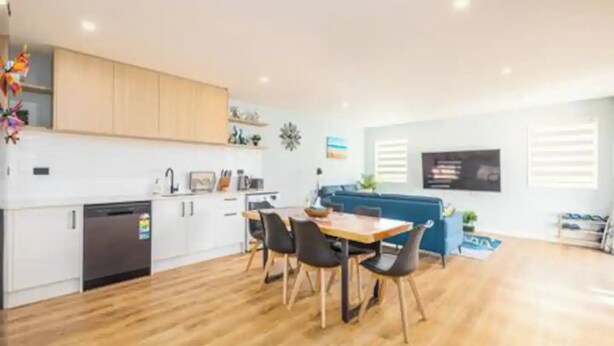 A modern kitchen with white cabinets, a dining area with a wooden table and chairs, and a blue sofa in a bright living space. - New, family friendly warm /3bedroom3bathroom/kingbed, mountain view/unitB (Lake Tekapo)