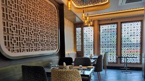 Interior de restaurante con diseño geométrico en la pared, sillas estampadas y grandes ventanales con vidrios decorativos.