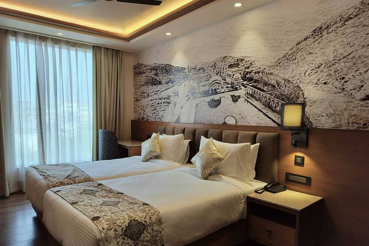 Ein Hotelzimmer mit einem großen Bett, zwei Nachttischen, einem Wandfernseher und einem Fenster mit Vorhängen.