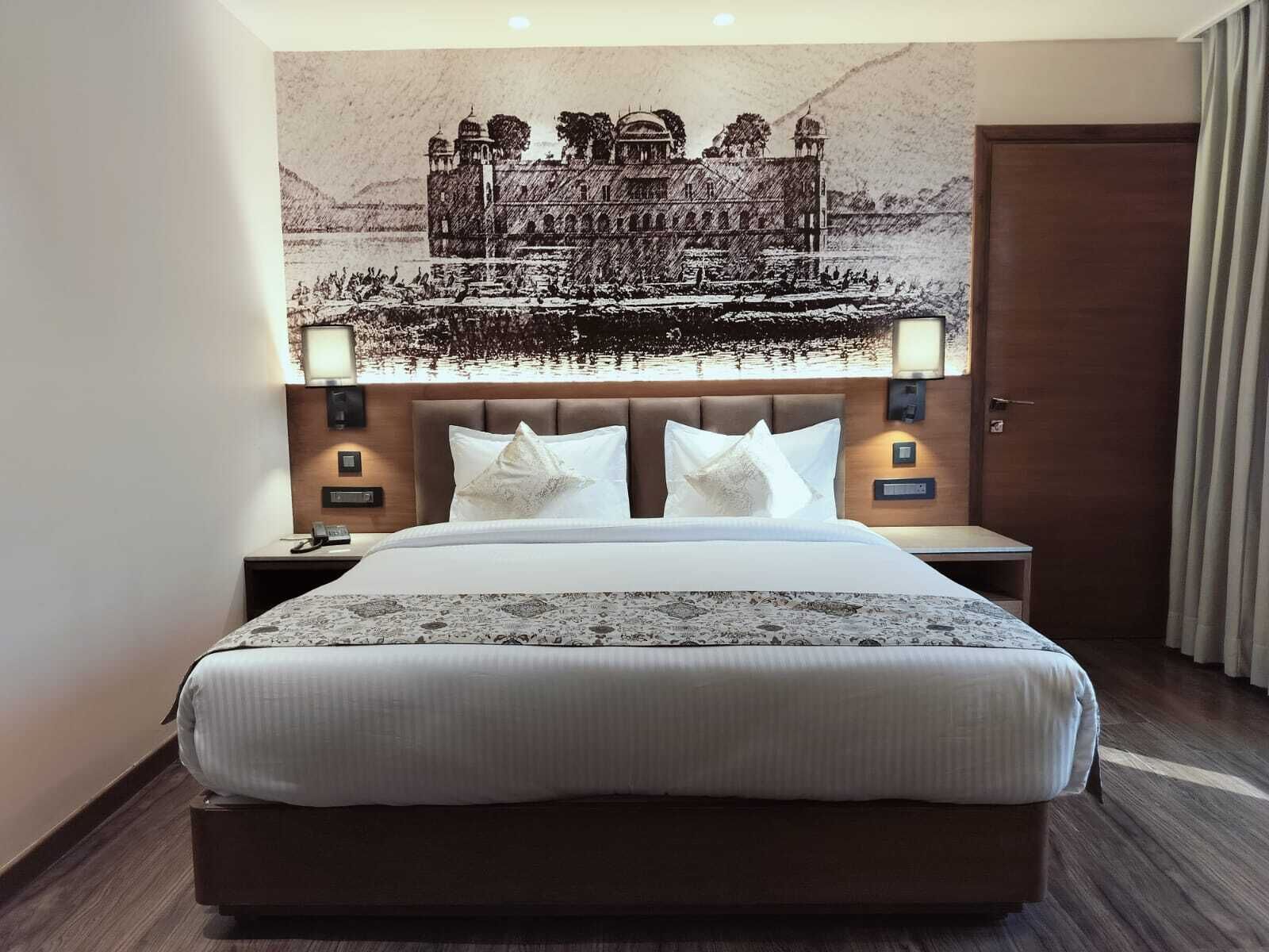 Quarto de hotel com uma cama grande, cabeceira com um mural, luminárias de cabeceira e uma porta de madeira.