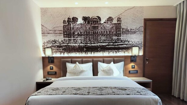 Ein Hotelzimmer mit einem großen Bett, einem Kopfteil mit Wandgemälde, Nachttischlampen und einer Holztür.