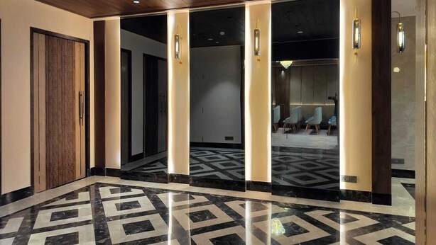 Un moderno vestíbulo de hotel con piso de mármol geométrico, techo de madera y puertas de vidrio que dan a un área de estar.