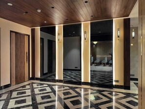 A modern hotel lobby with a geometric marble floor, wooden ceiling, and glass doors leading to a seating area. - Royal Lakshmi Palace (Jaipur)