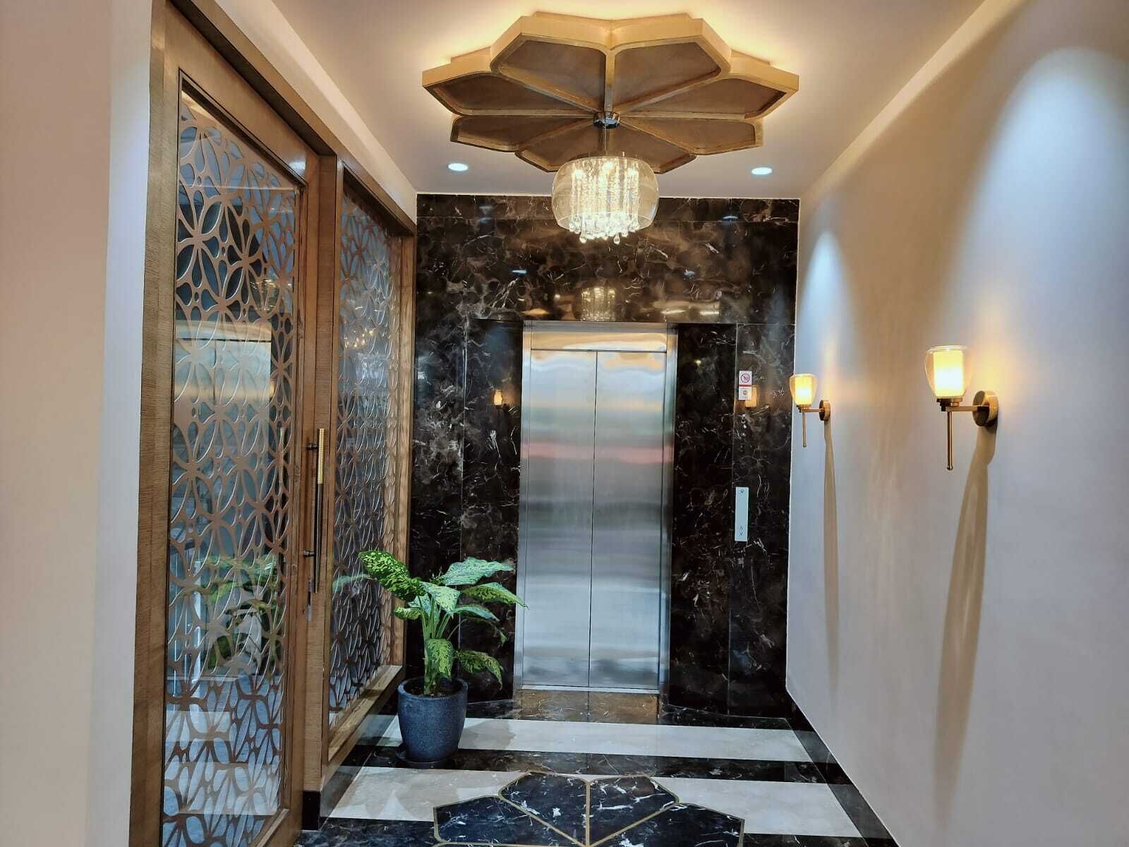 Een moderne lift met een metalen afwerking, een decoratieve plafondlamp en een potplant in de hal.