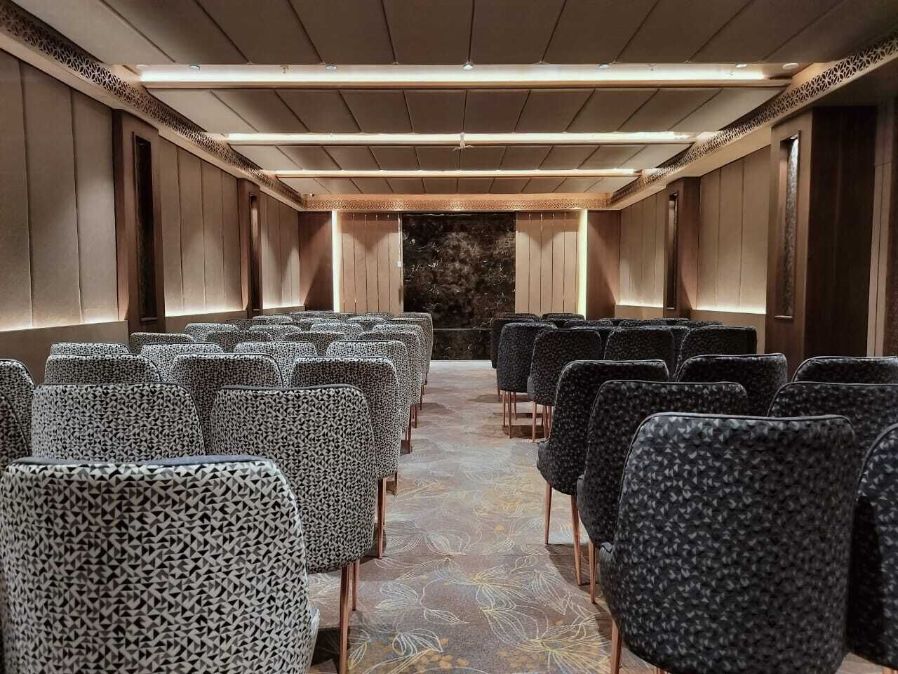 A conference room with rows of chairs, a patterned carpet, and a wooden ceiling.