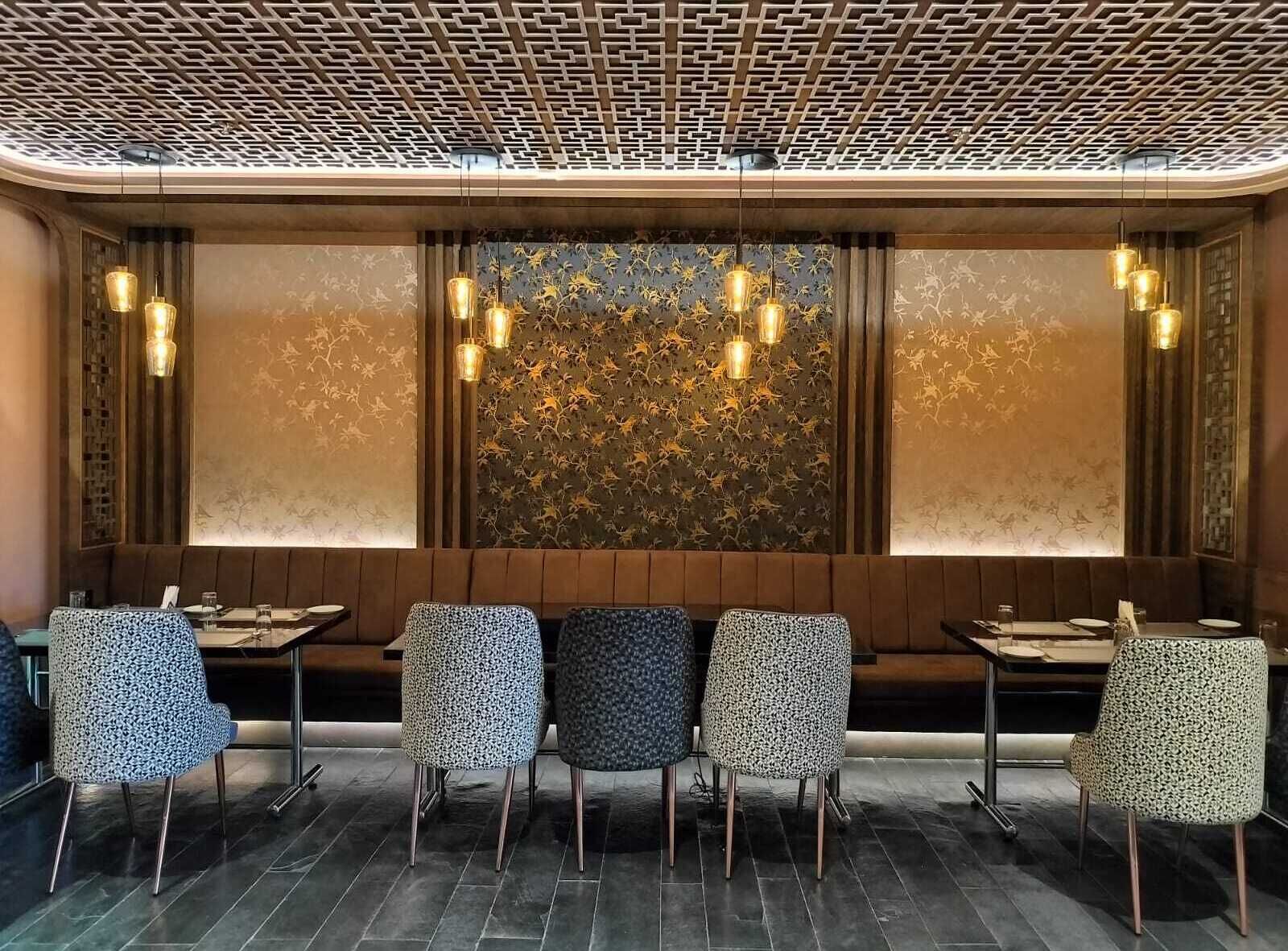 Interior de restaurante con pared estampada, asientos tipo banca de madera e iluminación colgante.