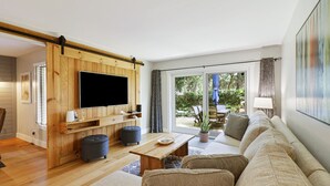 A modern living room with a wooden TV stand, a sofa, and a dining area with a table and chairs.