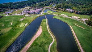 An aerial view of a golf course with multiple water hazards, a clubhouse, and surrounding greenery.