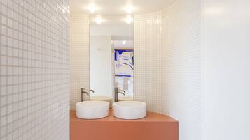 Un baño moderno con dos lavamanos, paredes de azulejos blancos y encimera marrón.