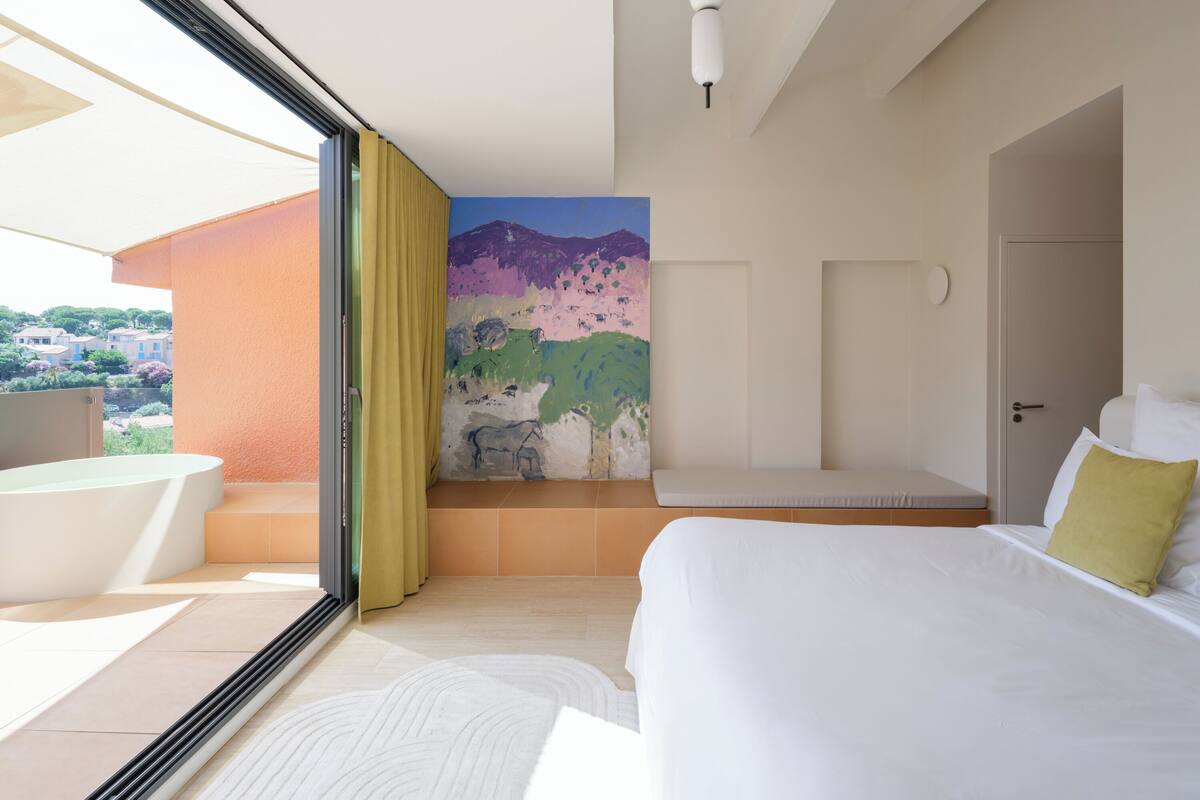 Ein Hotelzimmer mit Bett, Sitzgelegenheit, großem Fenster und Wandgemälde.