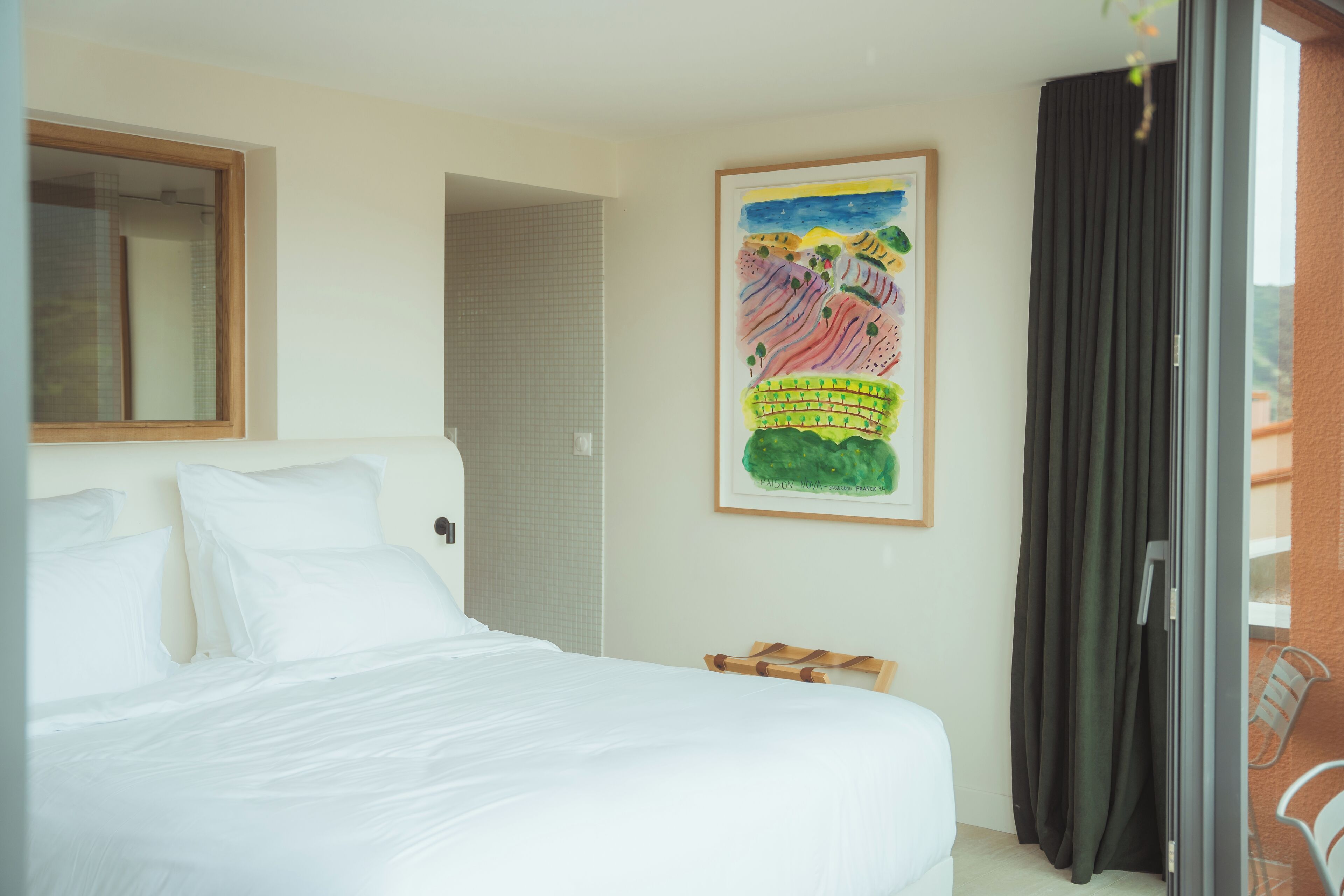 A hotel room with a bed, a window, a door, a painting, and a curtain.