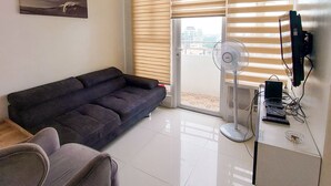 A modern living room with a dark sofa, a grey armchair, a ceiling fan, a flat-screen TV, and a painting on the wall. - Birch Tower Manila (Manila)