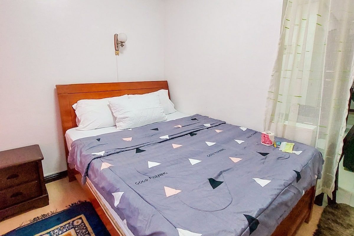 Une chambre à coucher avec un lit en bois, une table de chevet, un tapis à motifs et un luminaire au plafond.
