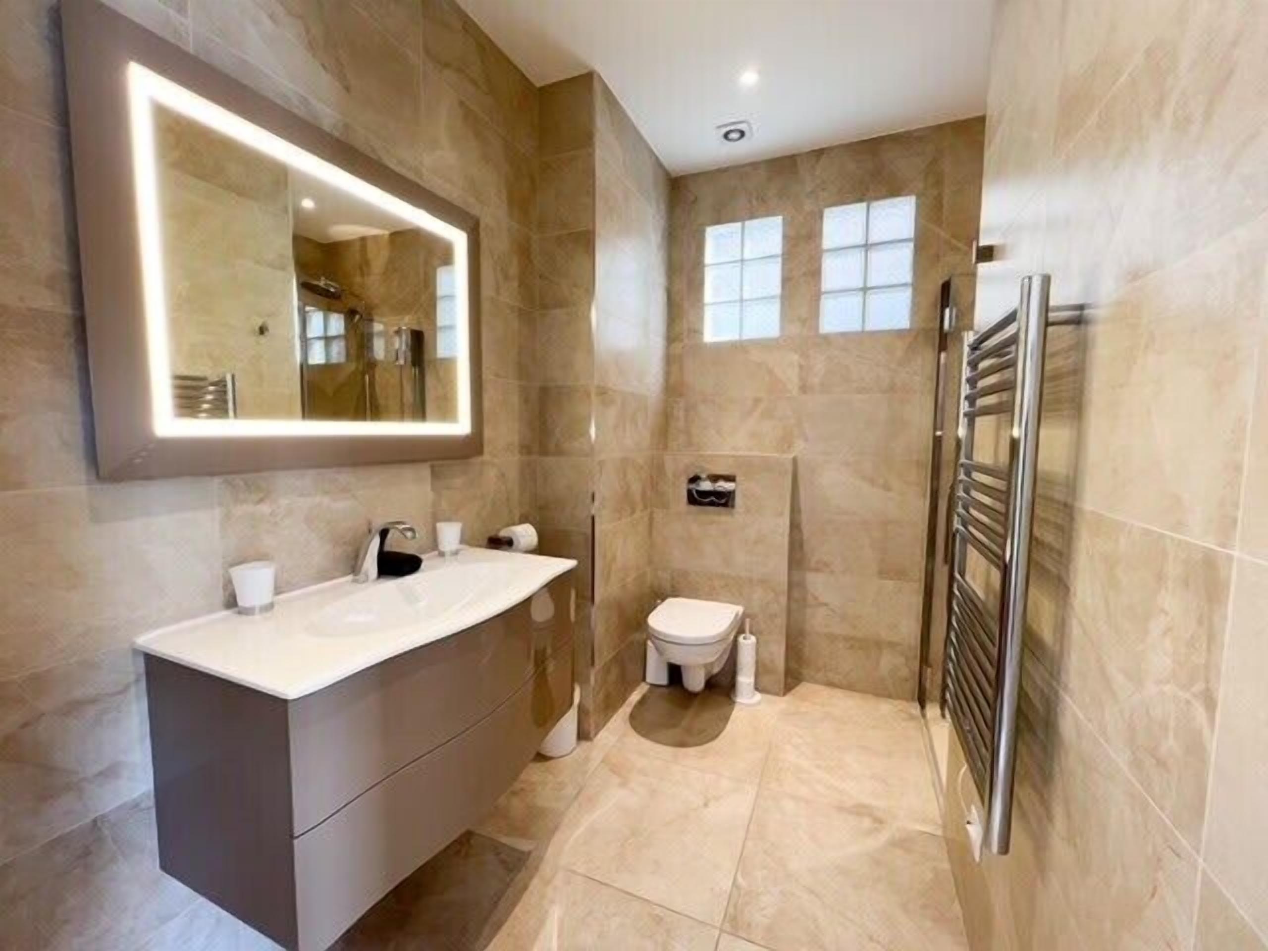 A modern bathroom with a large mirror, a walk-in shower, and a toilet.