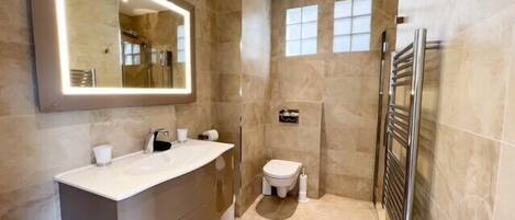 A modern bathroom with a large mirror, a walk-in shower, and a toilet.