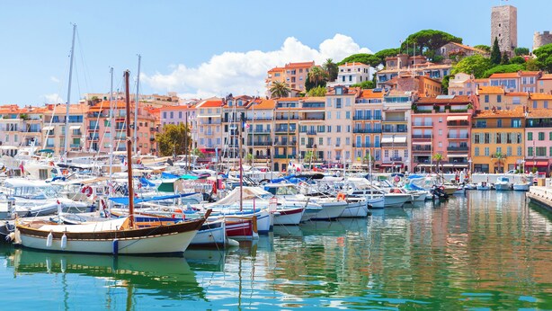 A marina with numerous boats docked, colorful buildings in the background, and a prominent tower on a hill. - Cannes: chic studio quiet in a secure residence 200m from the beaches (Cannes)