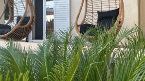 Two wicker chairs with black cushions outside a building with white shutters. - Milo by the sea (Analipsi)